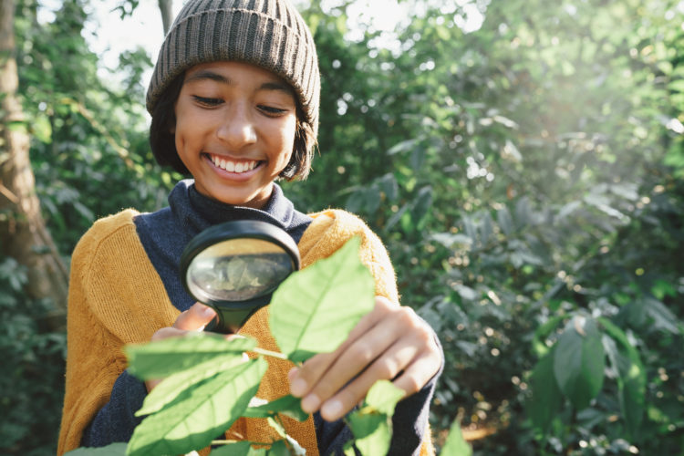 A young girl exploring nature with a magnifying glass and a happy smile In the midst of sunlight in the morning.