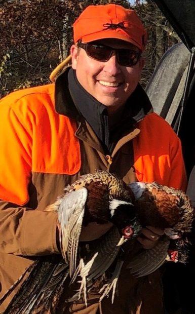 A hunter holds two pheasants. 