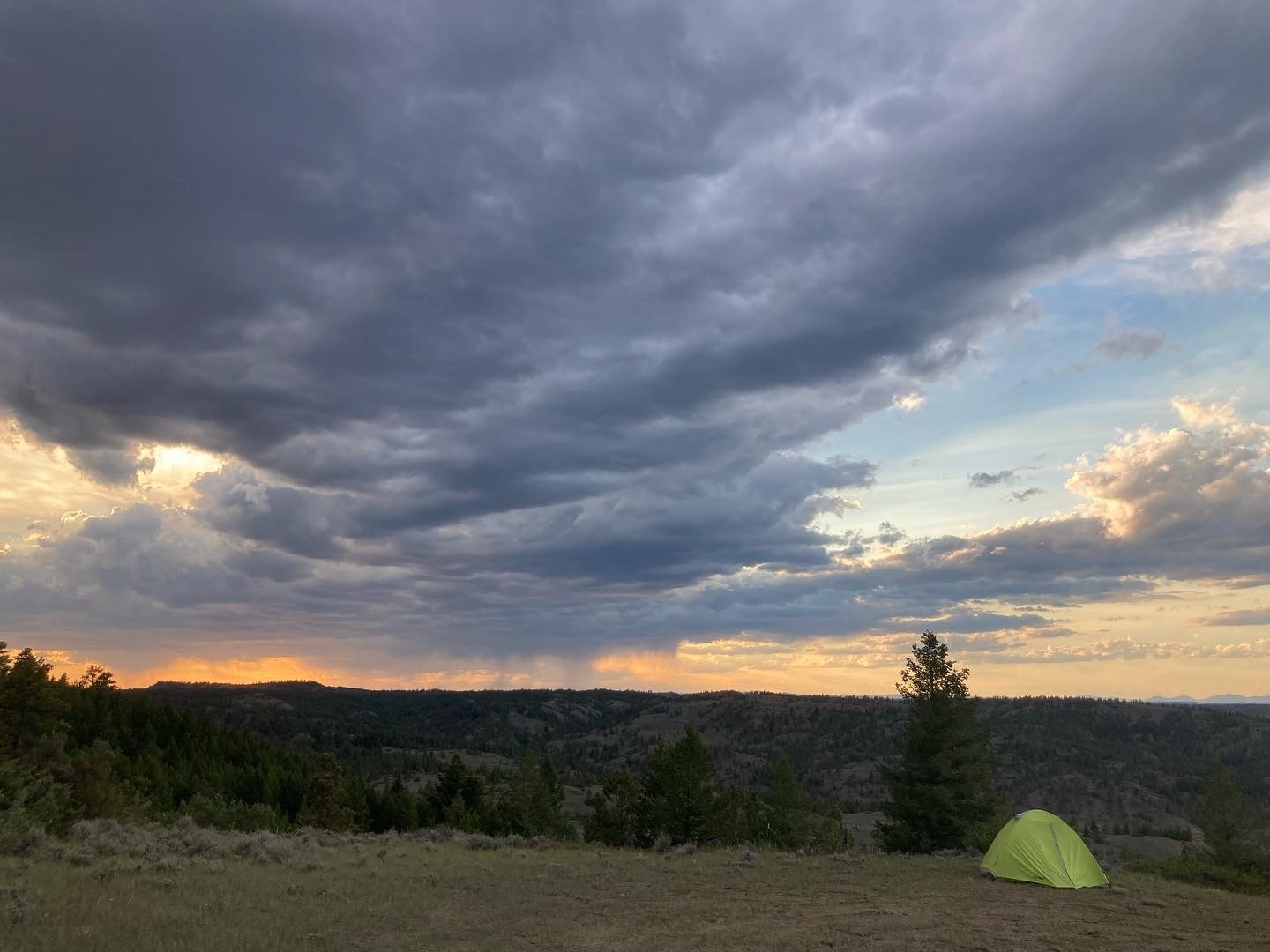 A tent at the designated campsite where volunteers camped with a rainstorm in the background at sunset. 