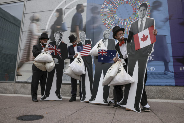 People dressed in top hats, suits, with fake mustaches and moneybags pose with cardboard cutouts of various world leaders.
