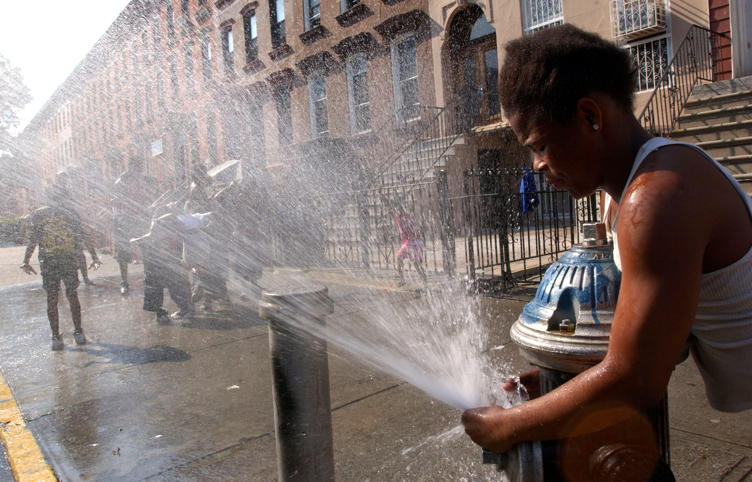 A person is redirecting the spray from a fire hydrant on a sidewalk. Other children are standing nearby.