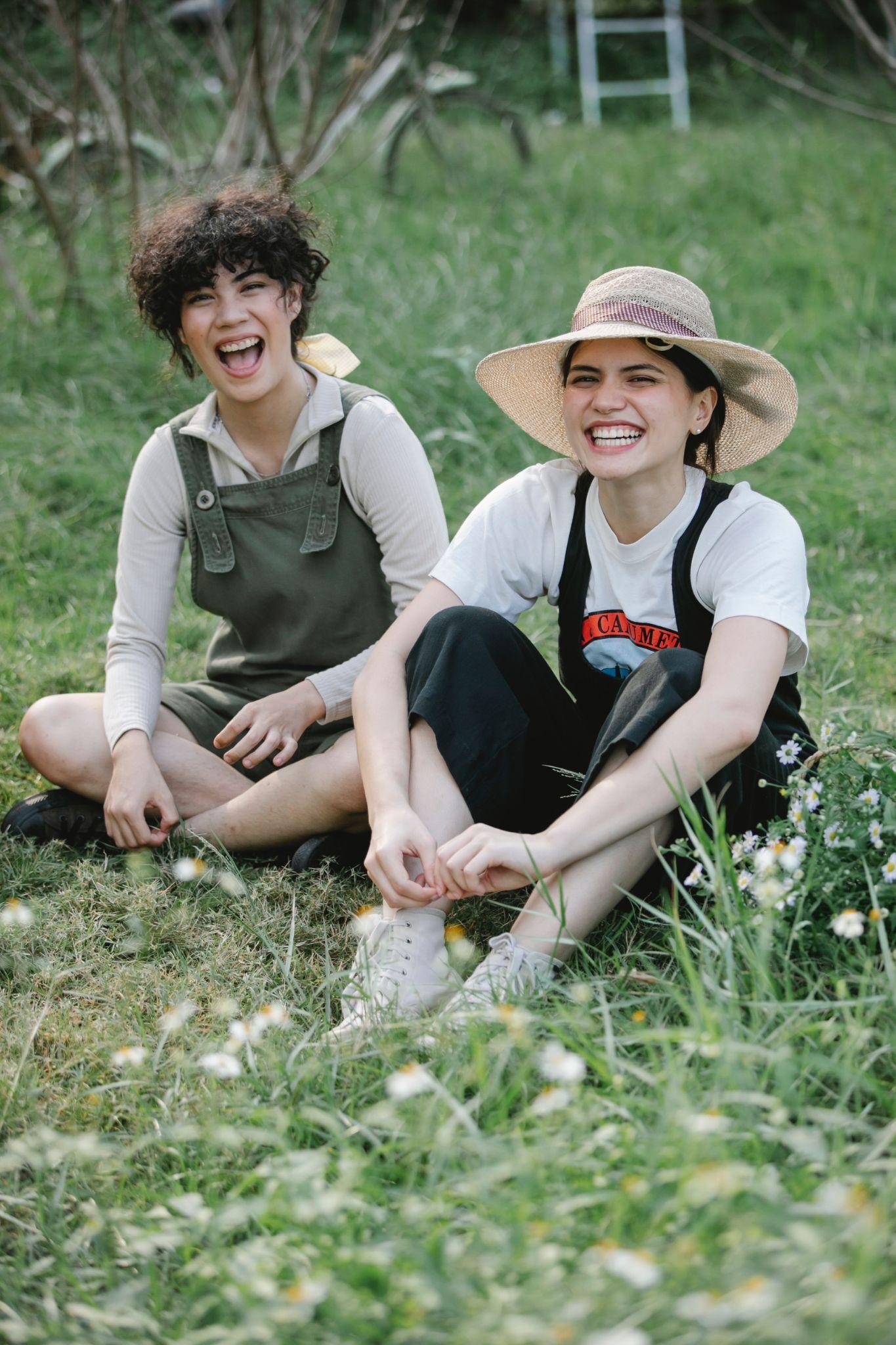 Two people are sitting in a meadow, laughing together.