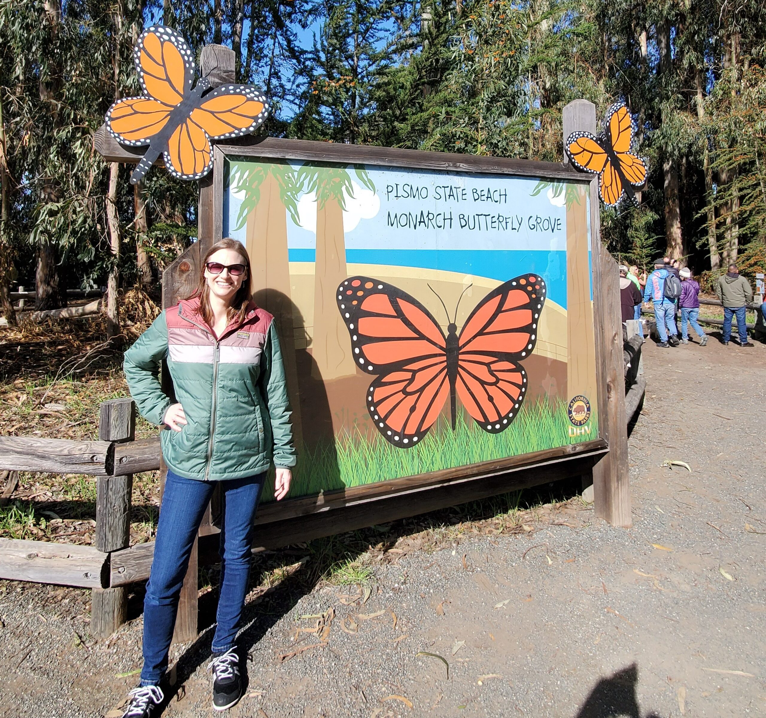A woman stands in front of a sign featuring large monarch butterfly artwork. 