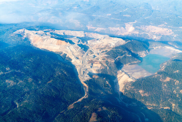 An aerial view of mountains, some covered in trees and some stripped, and a large body of water.