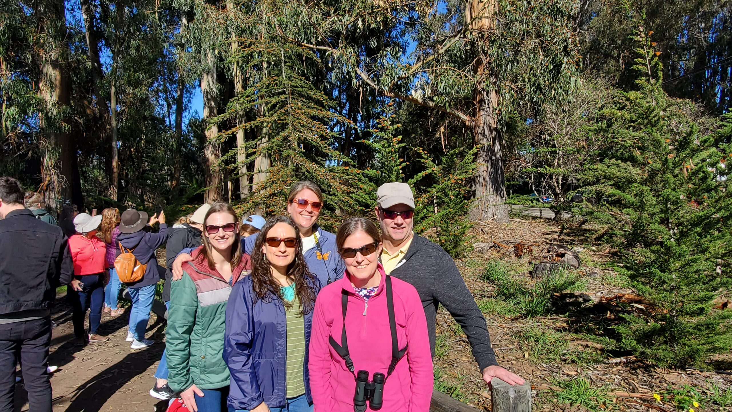A group of people stand together for a photo in a forested area.