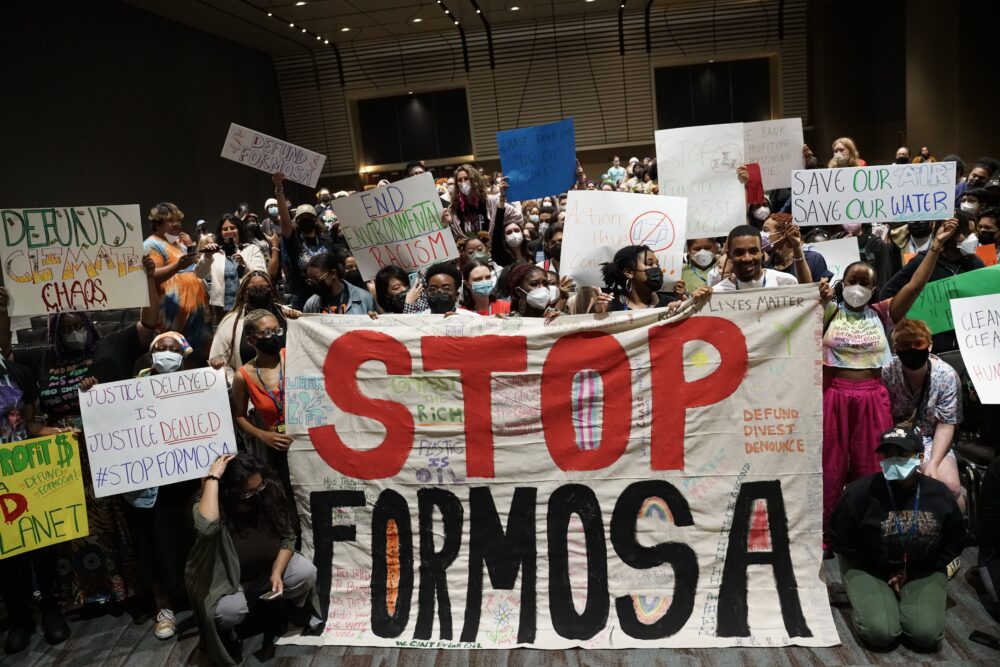 A crowd of people with signs and banners pose for a photo. The biggest banner reads, "STOP FORMOSA".