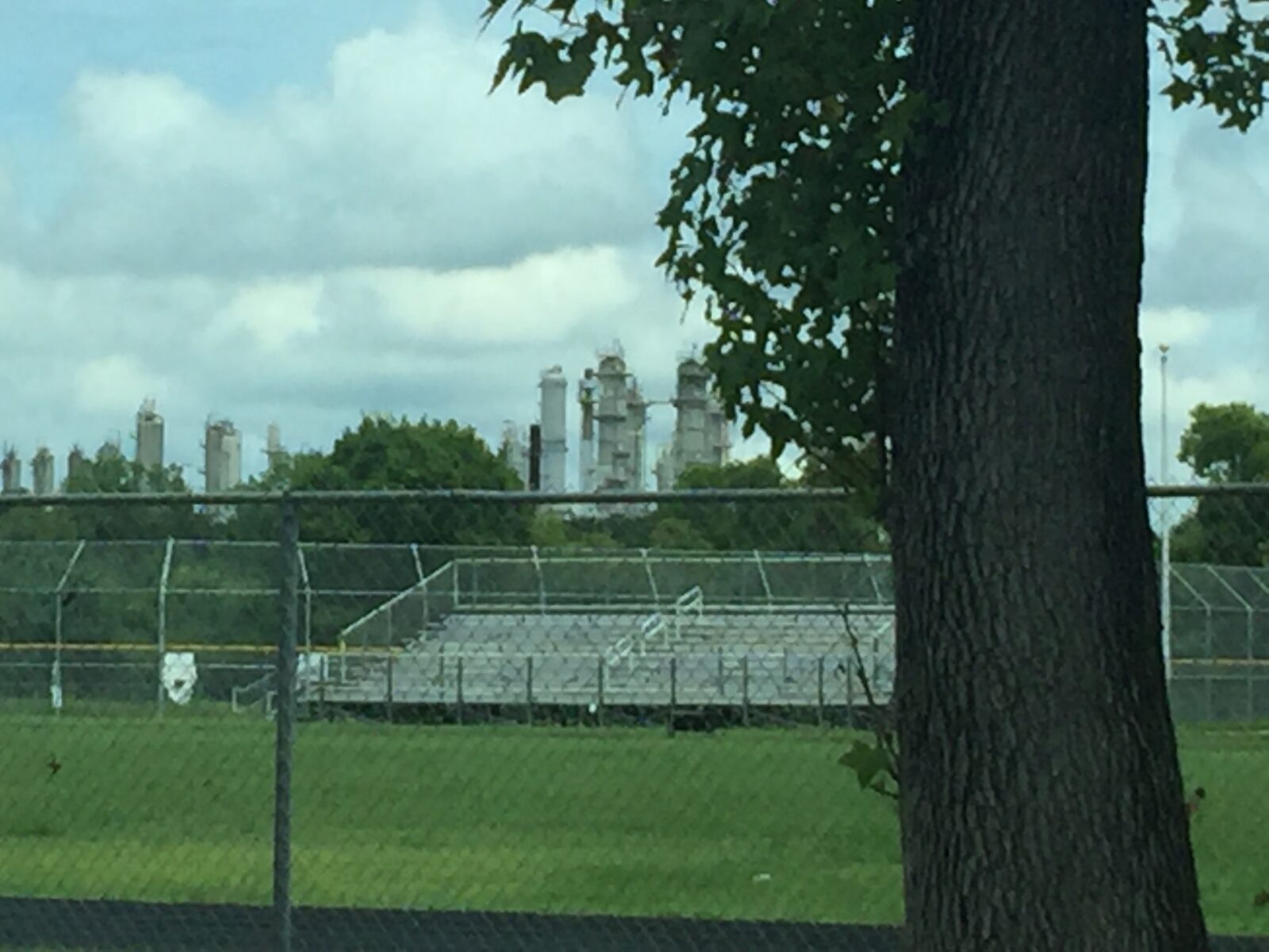A school sports field can be seen in the frame; in the background there are smoke stacks releasing air pollution into the sky.