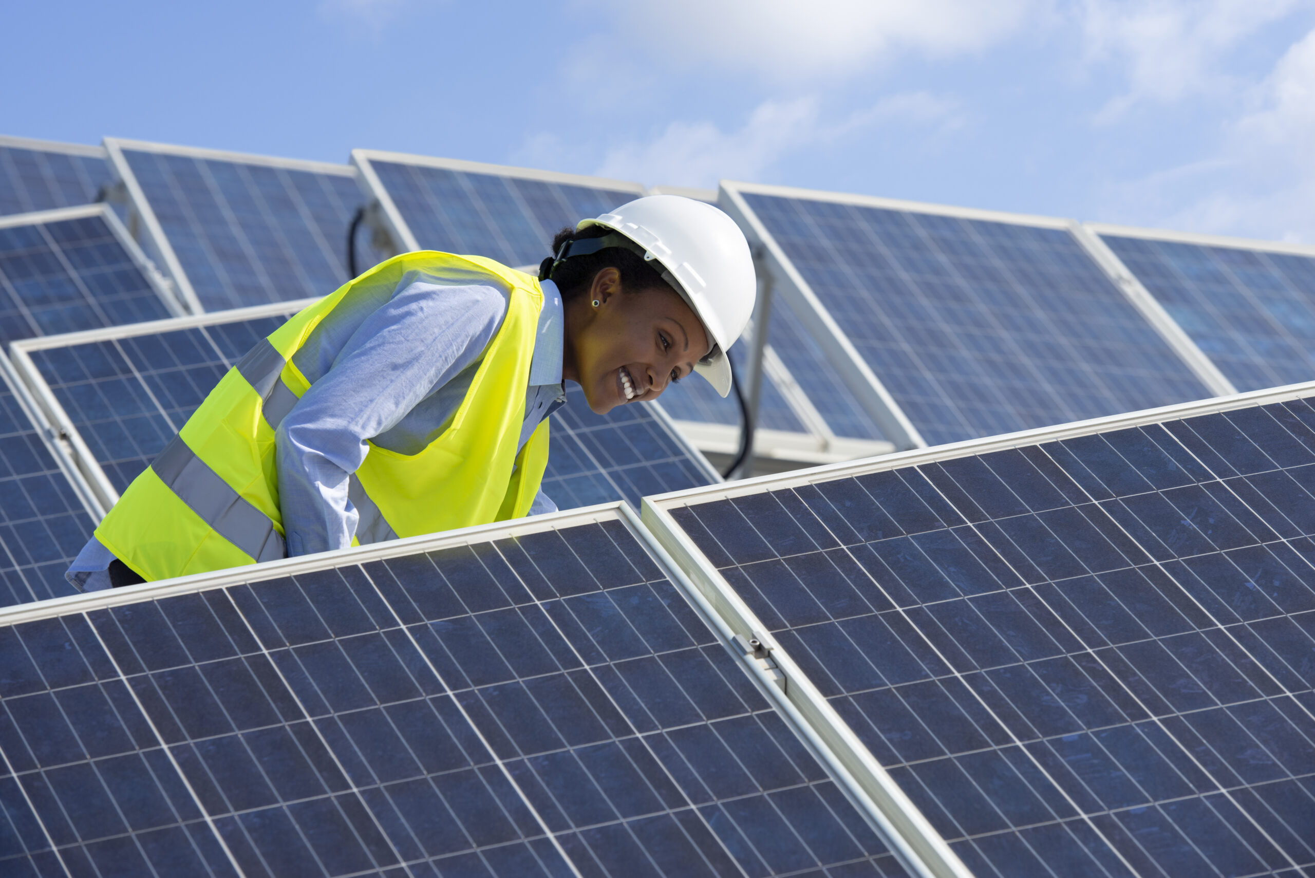 A person with a hard hat and reflective vest on is checking solar photovoltaic panels.
