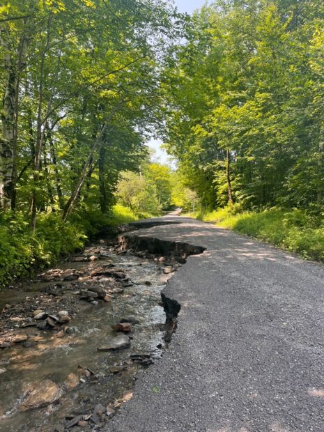 A dirt road appears to be eroded and damaged by floodwaters.