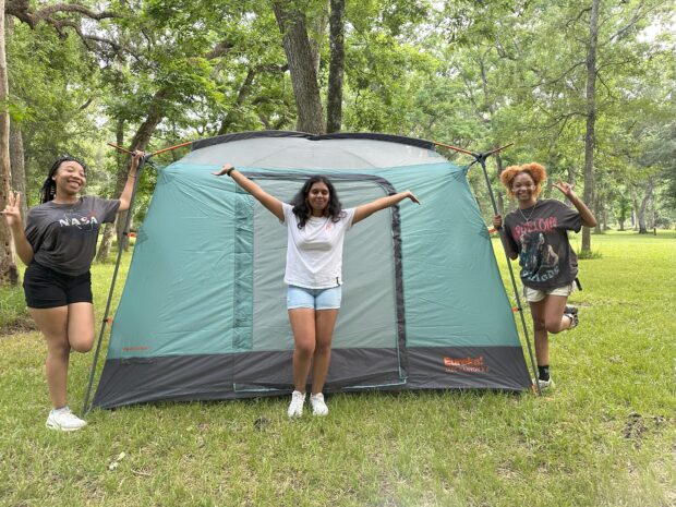 Three people pose in front of a tent outside.