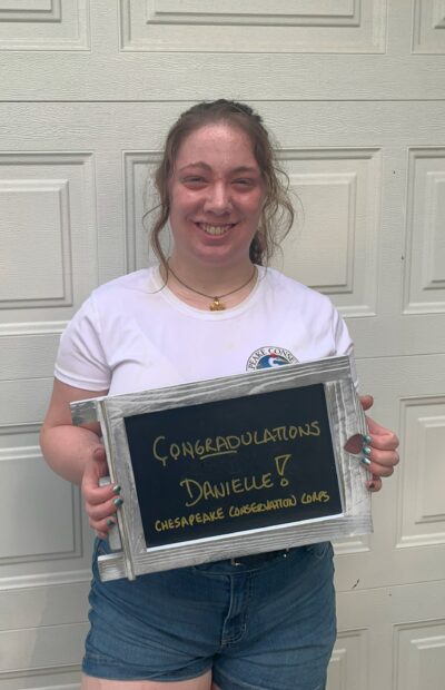 A person stands holding a sign reading, "Congradulations Danielle! Chesapeake Conservation Corps"