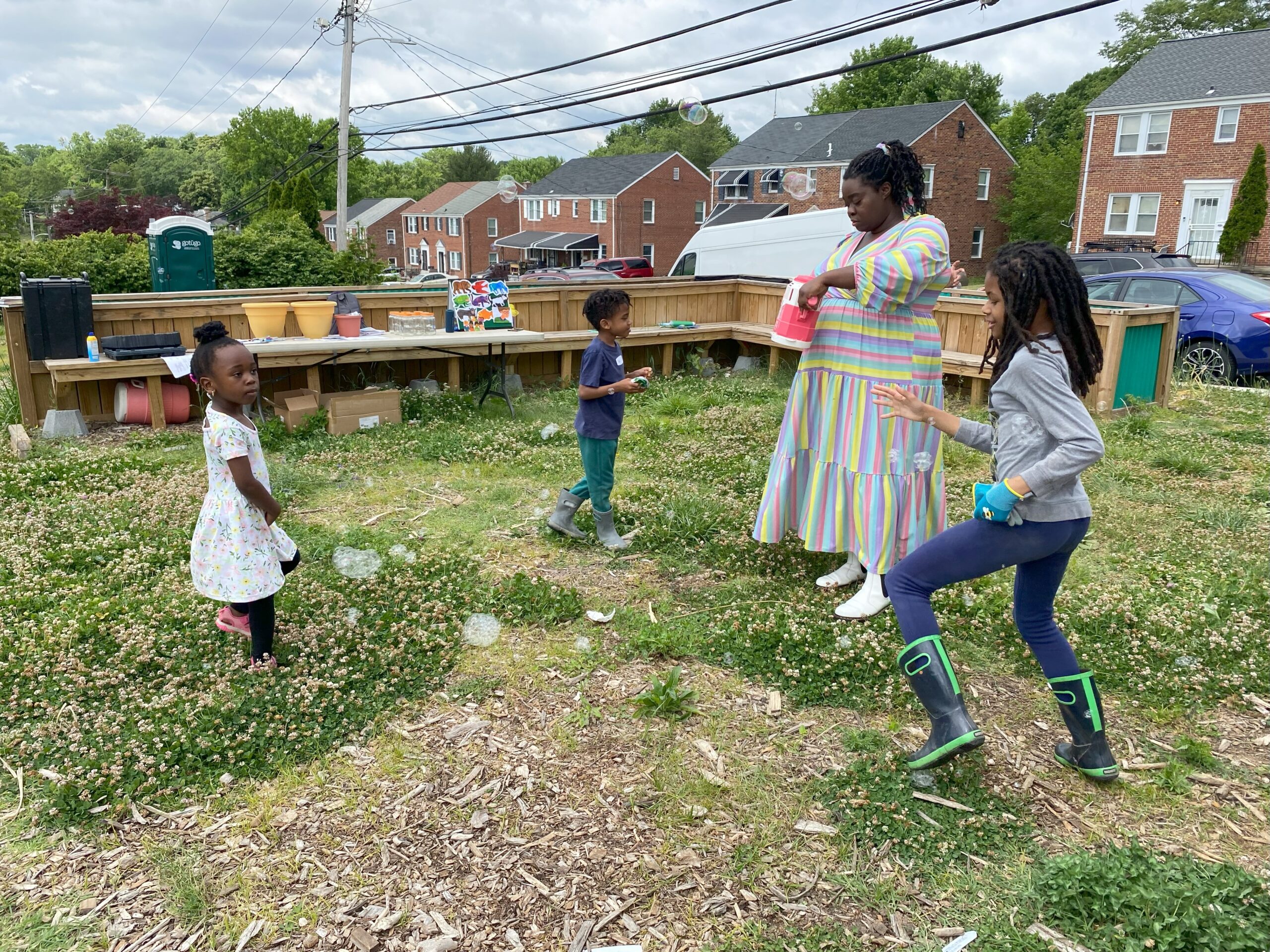 An adult and three children are outside playing with a bubble machine.