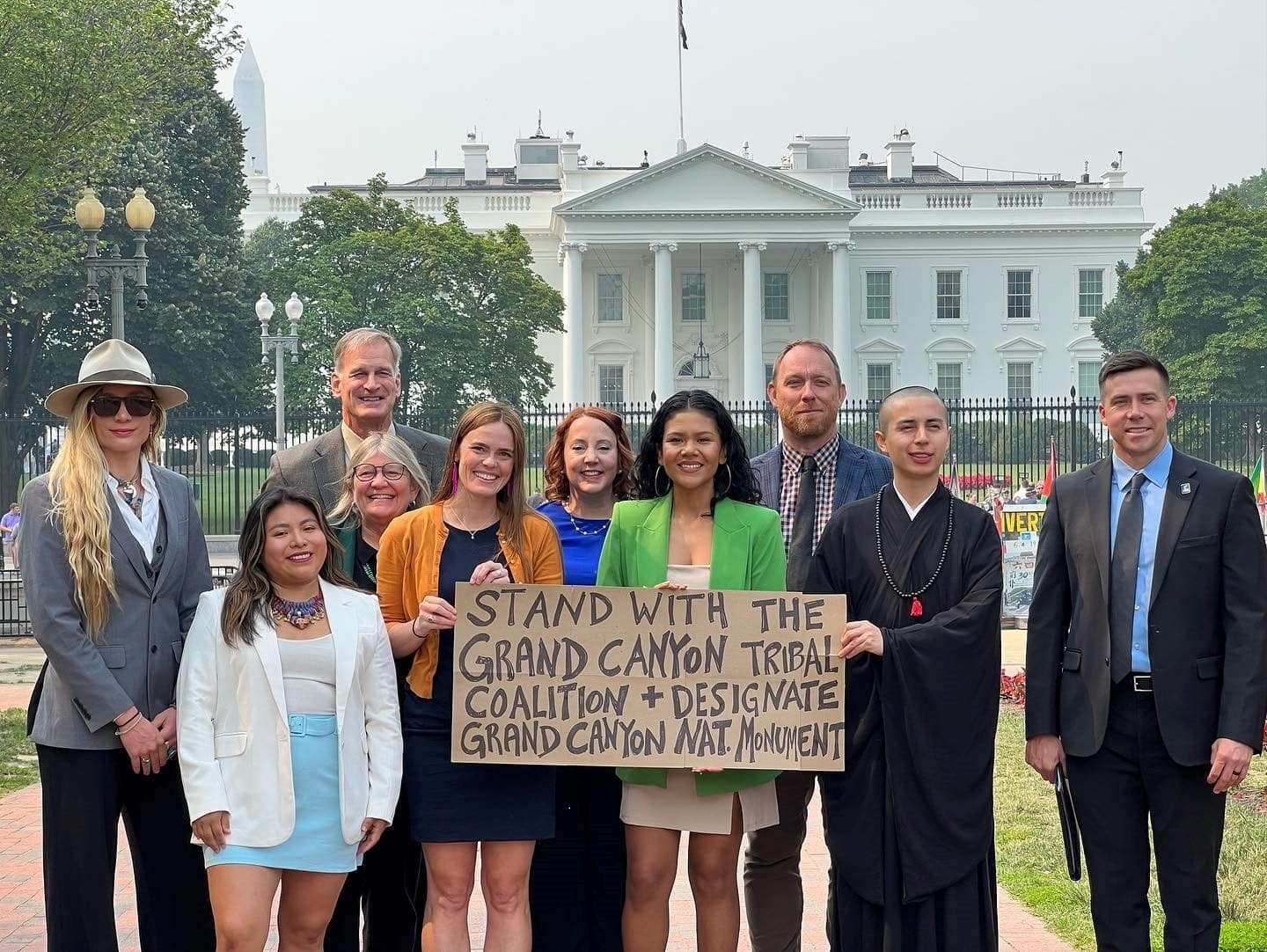 A group of people stand in front of the While House with a sign reading, "Stand with the Grand Canyon Tribal Coalition + designate Grand Canyon Nat. Monument