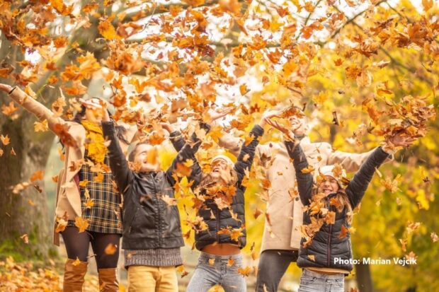 People throw yellow and orange leaves up into the air.