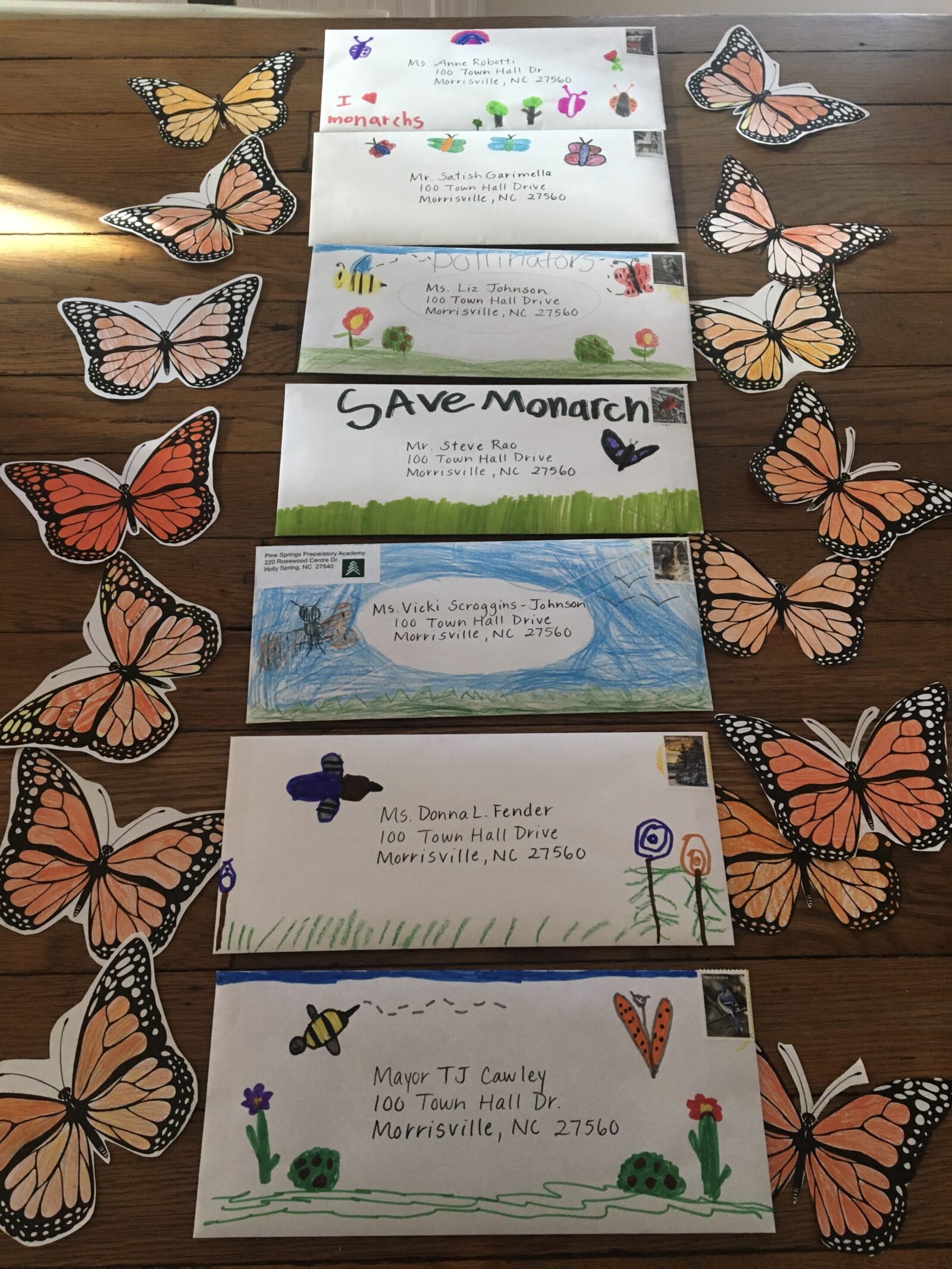 Several handwritten envelopes lay on a table surrounded by monarch butterfly stickers.