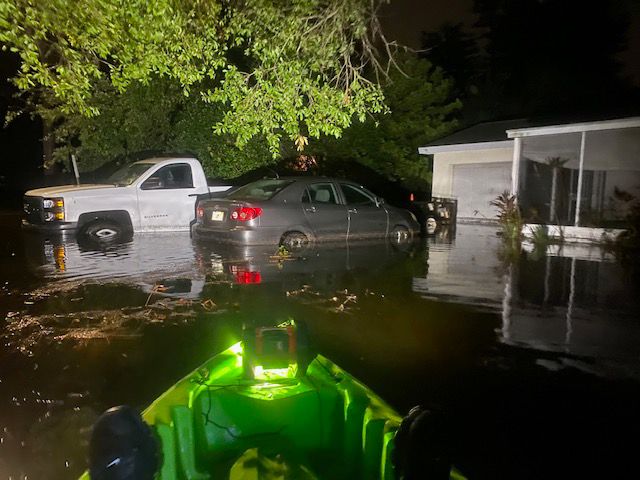 Flood waters inundate vehicles near a home.