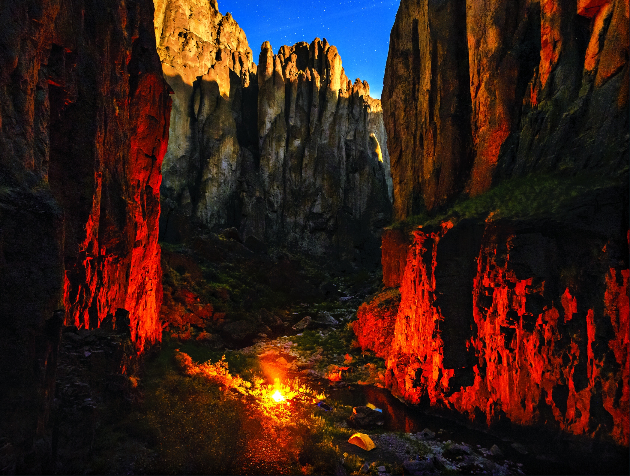A small fire burns in a large canyon at night.