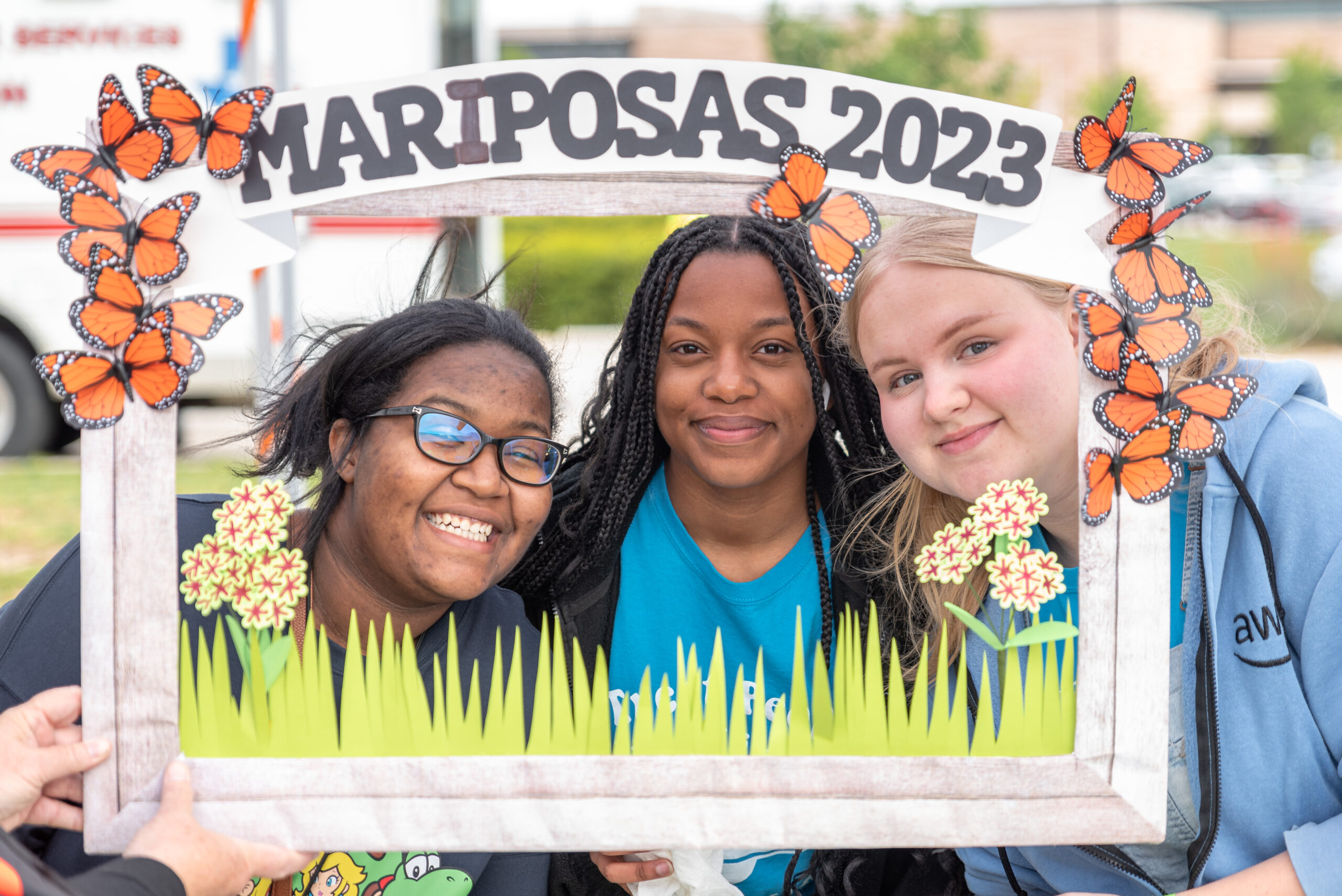 Three people pose for a photo with a photo frame prop that reads, "MARIPOSAS 2023".