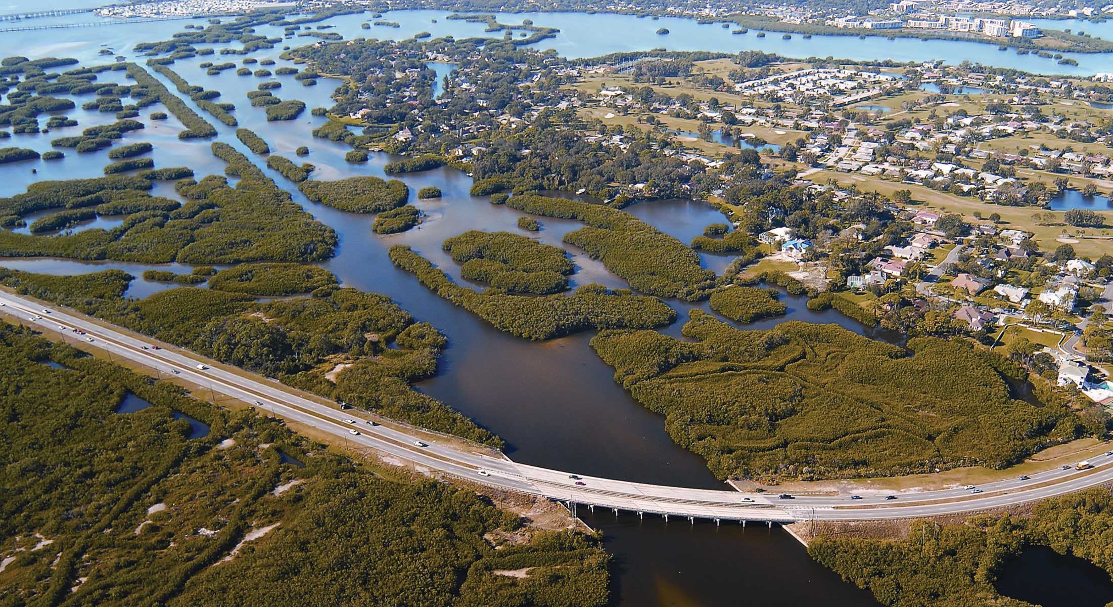 Aerial view of a watery landscape and a highway bridge crossing over a large channel of water.