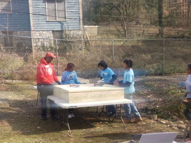Young volunteers wearing blue "Earth Tomorrow" t-shirts work on a wooden garden box.