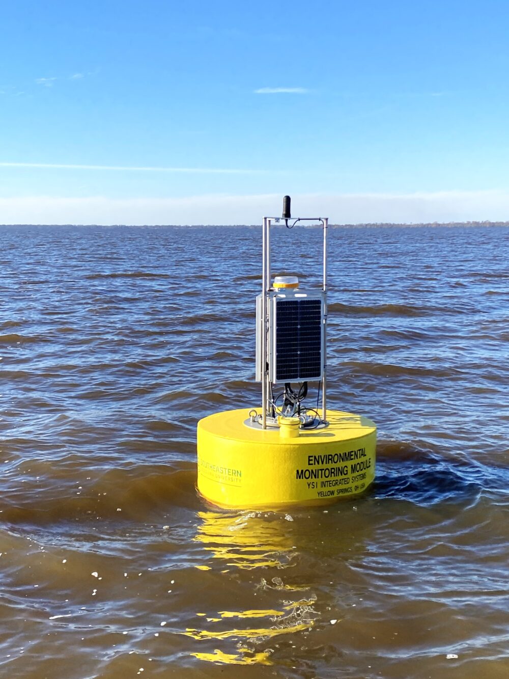 A yellow apparatus floats in the water. It is labeled, "Environmental Monitoring Module".