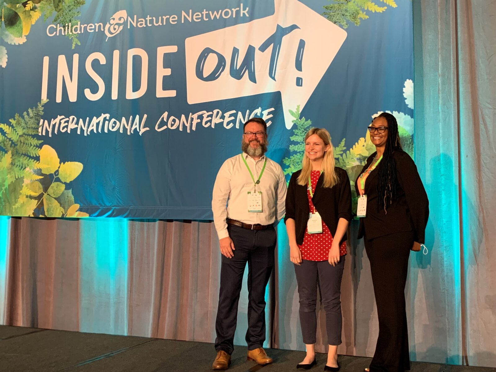 Three people stand on a stage in front of a banner that reads, "Inside Out! International Conference".