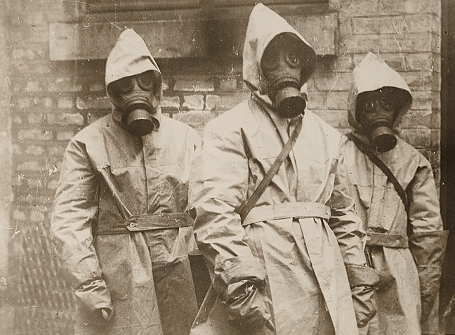 Sepia photograph of three people wearing body suits and gas masks.