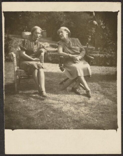 Old sepia photograph showing two people sitting on chairs on a lawn.