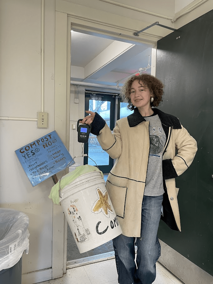 A person holds a white bucket with a handmade sign on it that details how to properly compost.