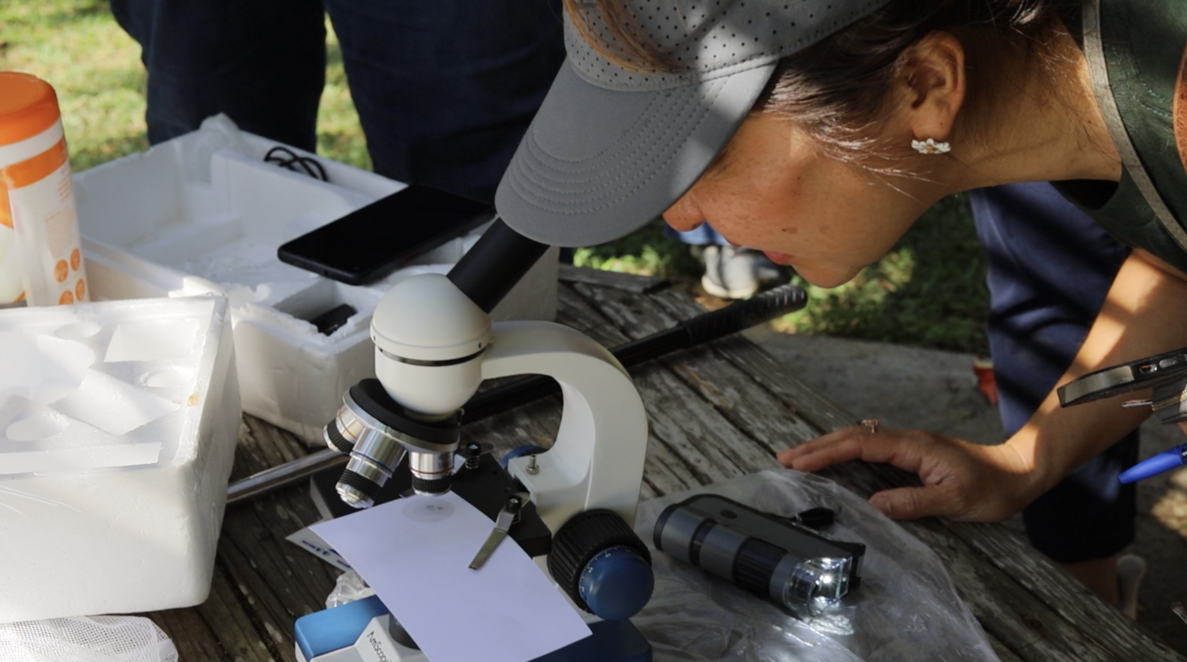 A person wearing a cap looks into a microscope.