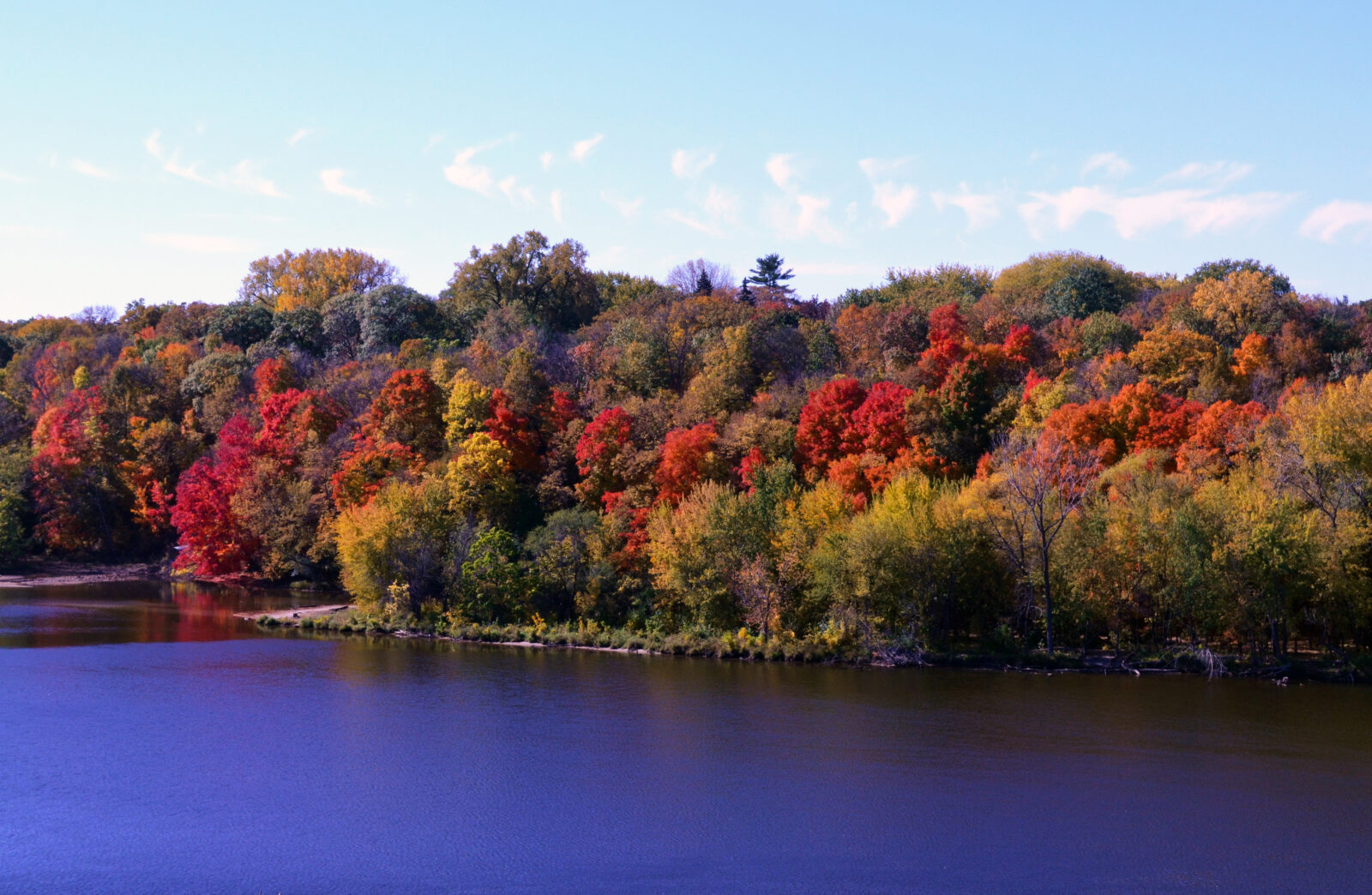 Wide view of a river with red, golden, and green trees on its banks.