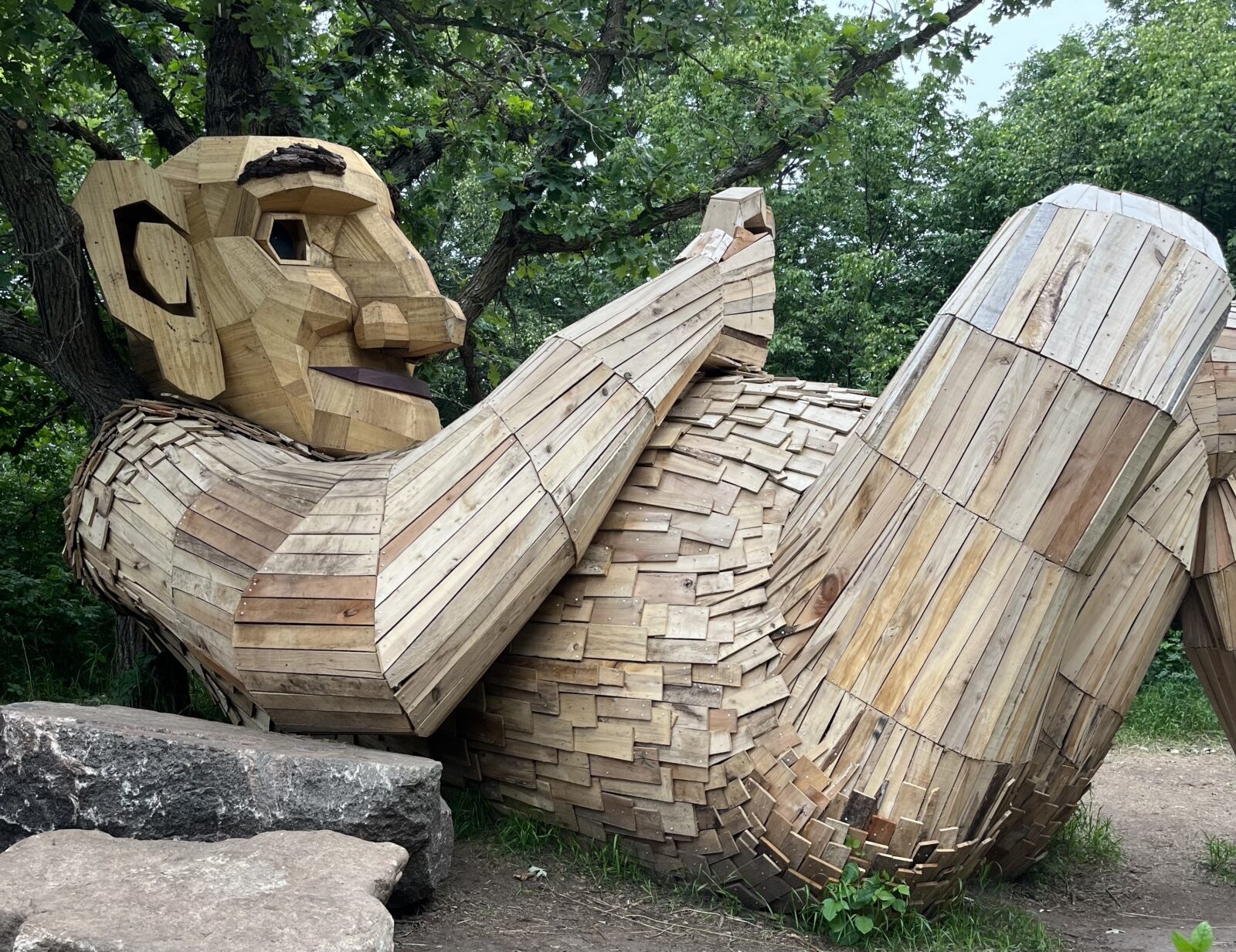 A large sculpture made out of wood depicts a troll resting on its back.