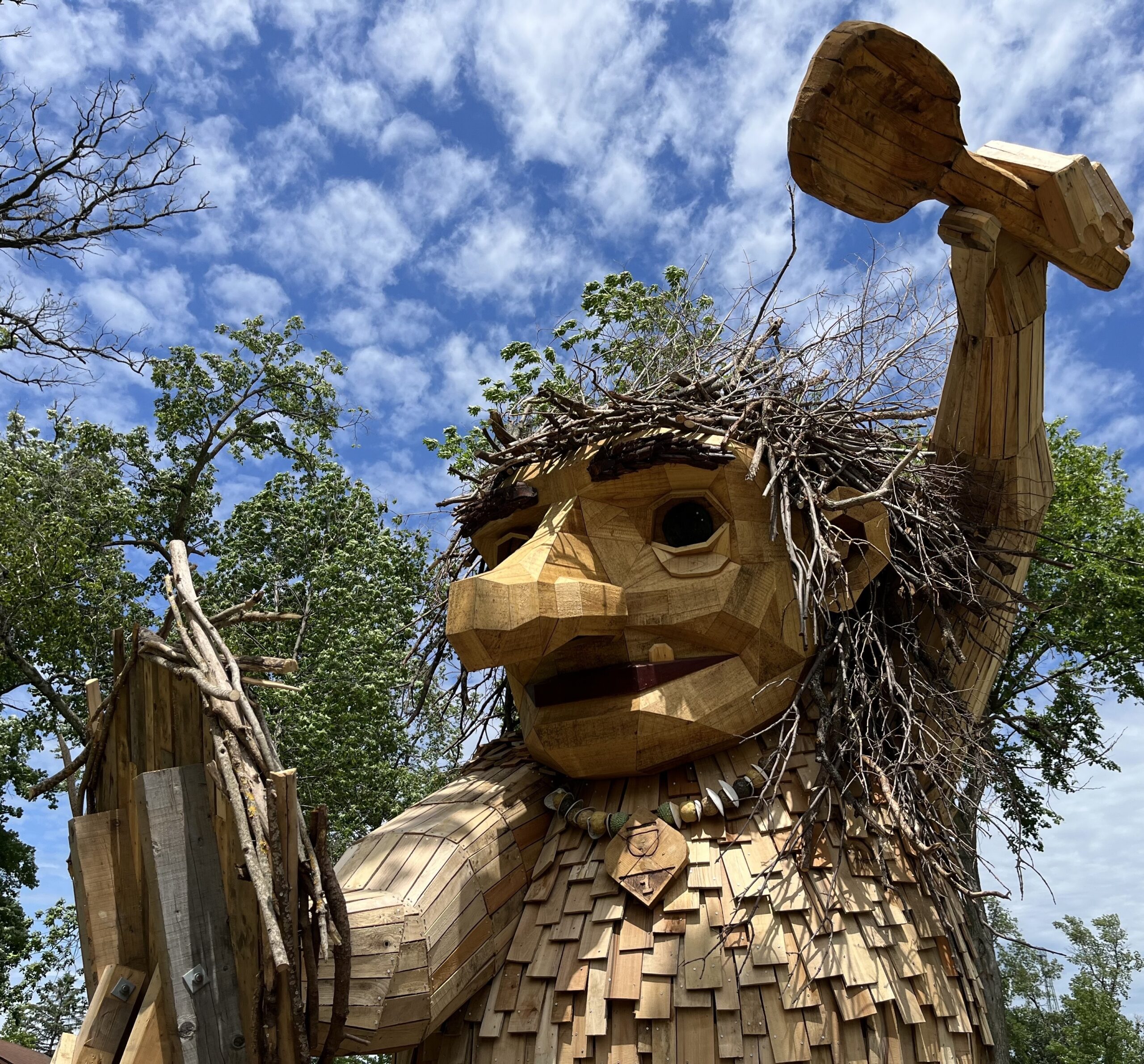 A wooden sculpture depicts a troll raising its arm over its head, holding something in its hand.