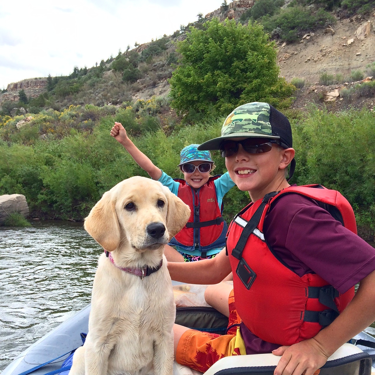 Two children and a puppy are in a small boat, smiling at the camera.