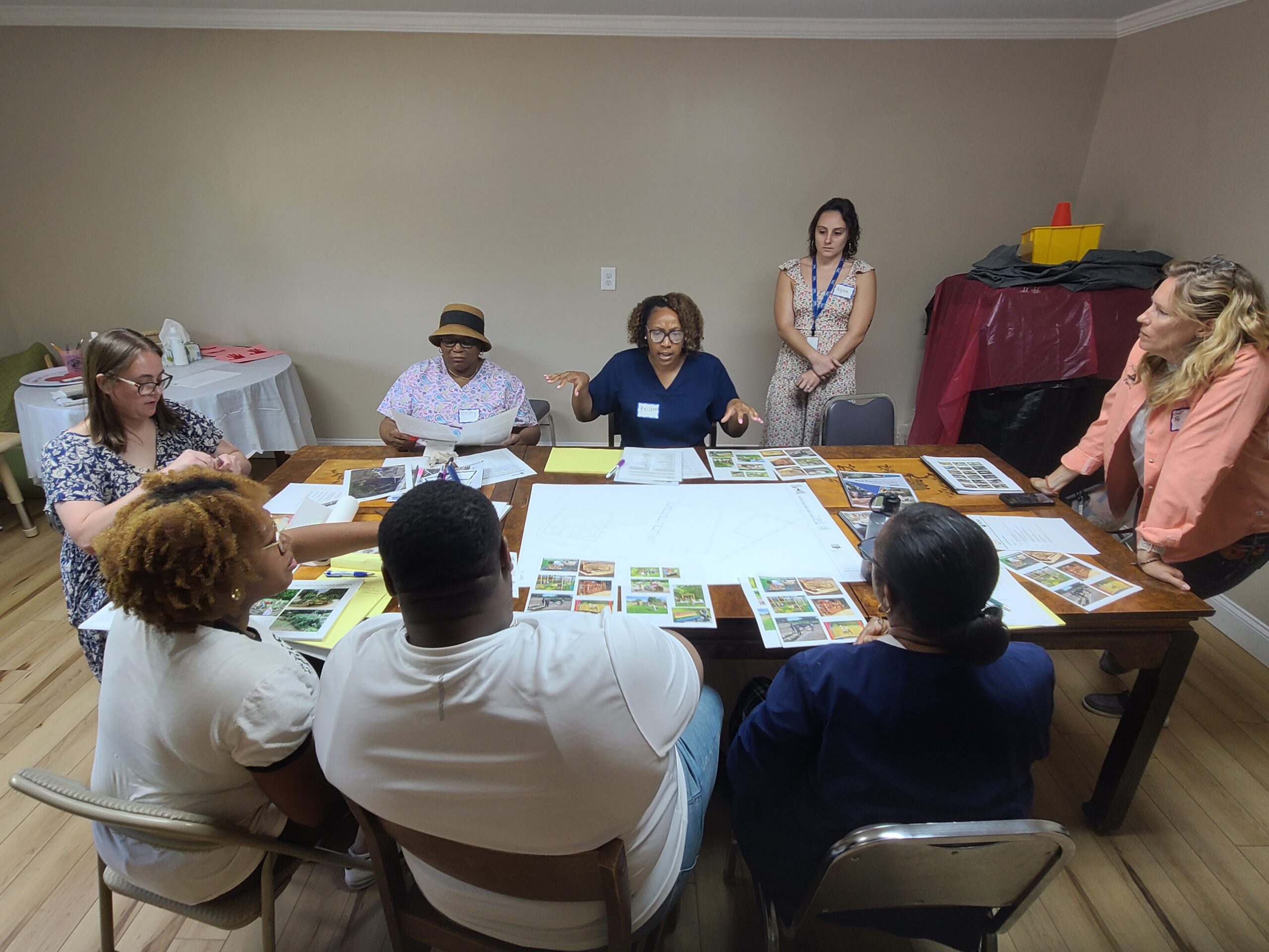 A group of people sit around a table with a large poster board and several pictures.