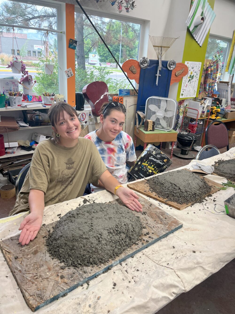 Two people sit at a table with wet concrete formations on it.