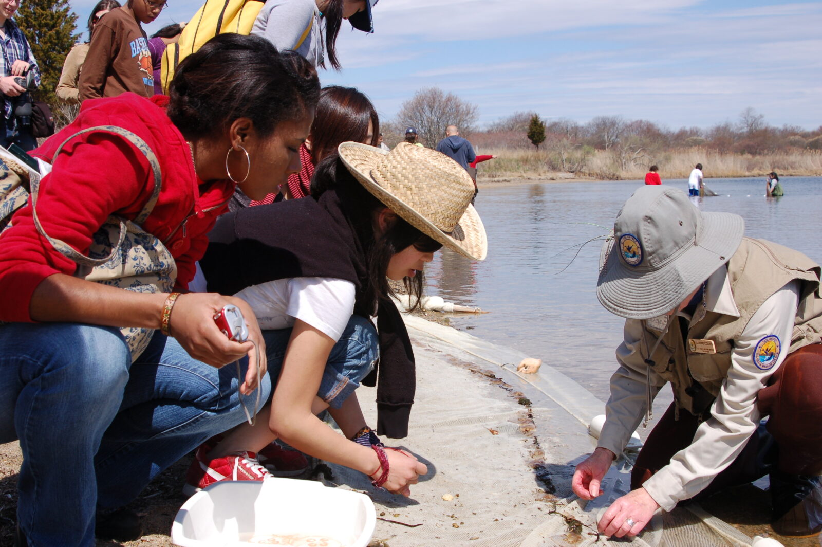 Older students observe a park ranger near a body of water.