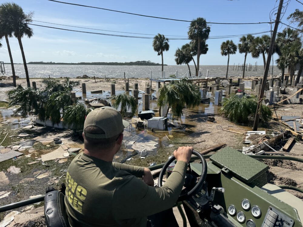 A person wearing uniform and driving a utility vehicle looks out at destruction and debris from a storm.