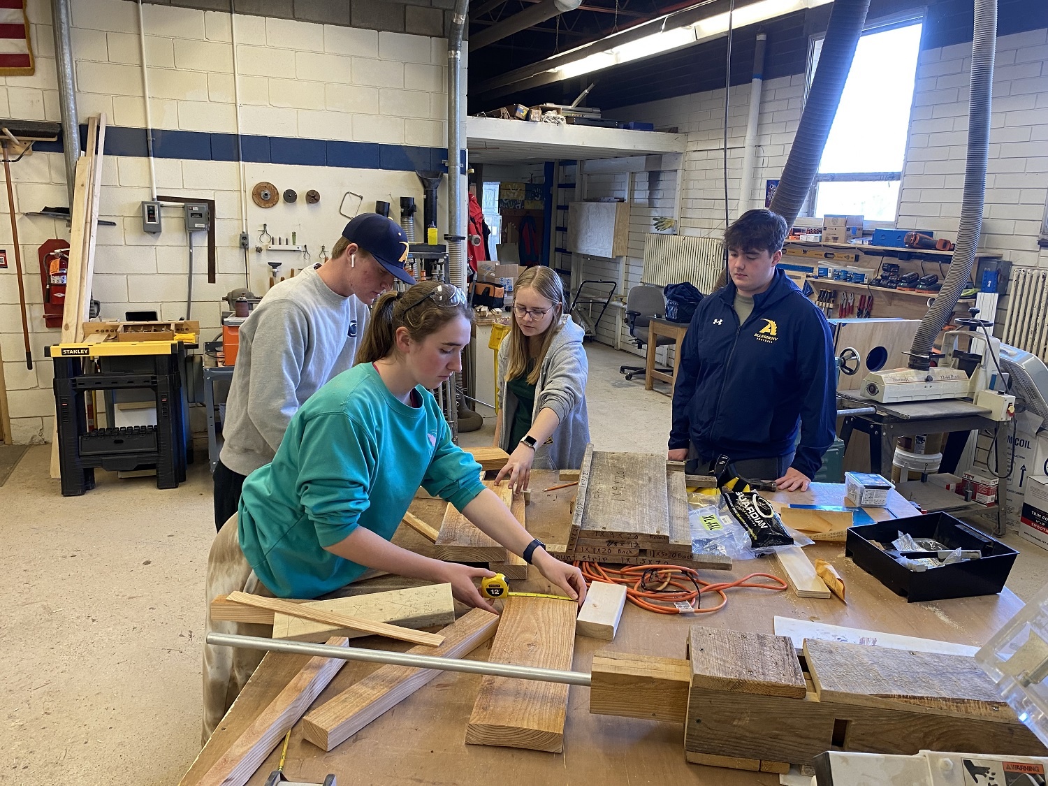 A group of young people build small structures in a classroom woodshop setting.