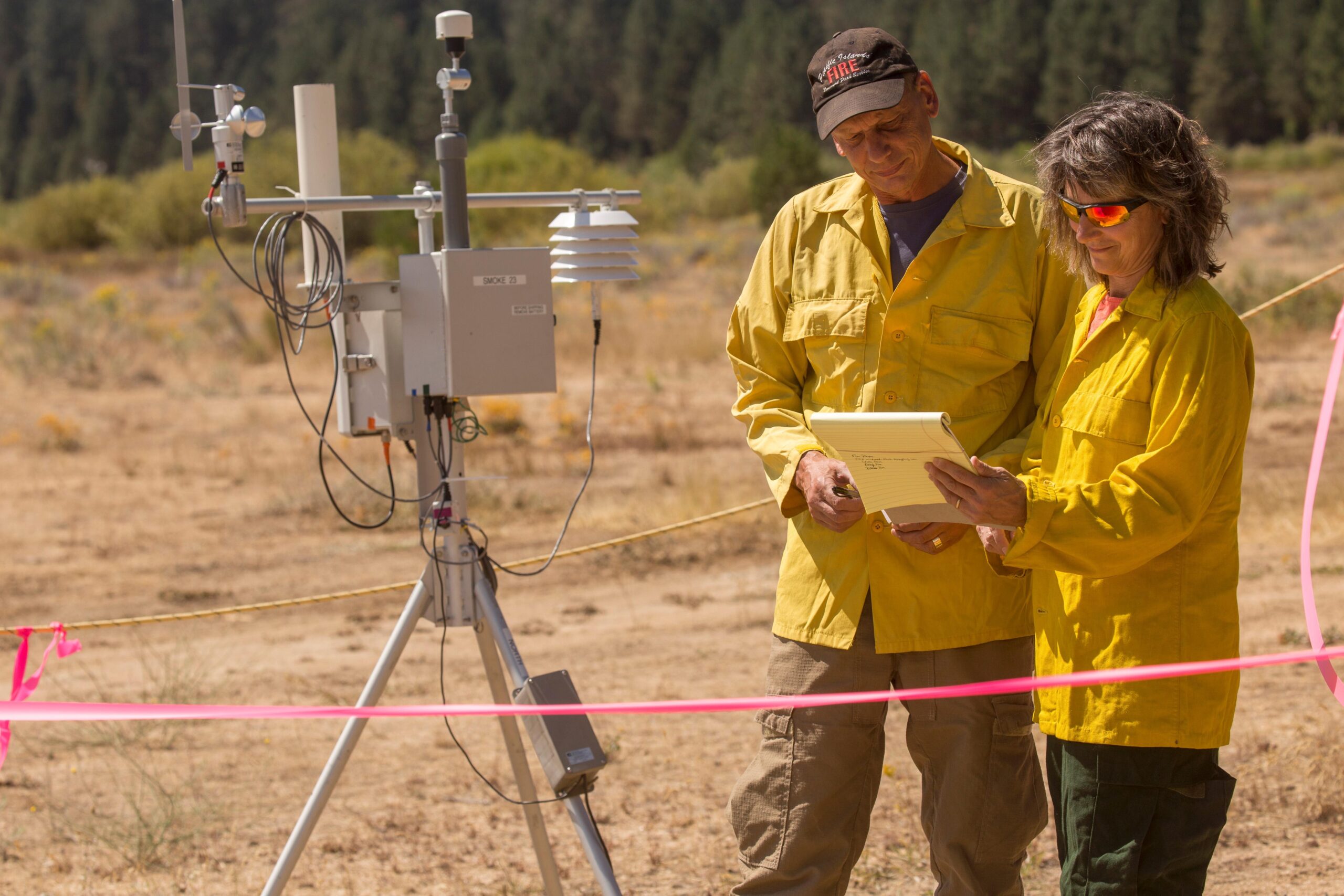 Two people stand near an air quality monitoring apparatus.